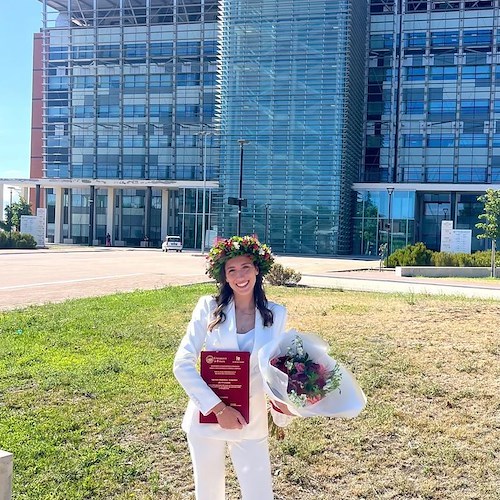 Maria Caso, elegante e sorridente, festeggia sotto il sole di Foggia con il fascicolo della sua tesi in primo piano